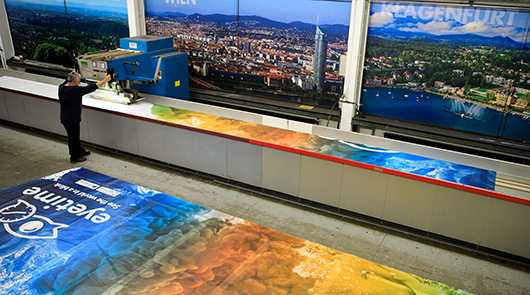 Großformatdruckerei mit Wien- und Klagenfurt-Motiven. Druckmaschine im Einsatz. Über uns.