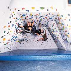 Kletterwand mit Prallschutzmatte. Zwei Personen beim Klettern an der Wand.