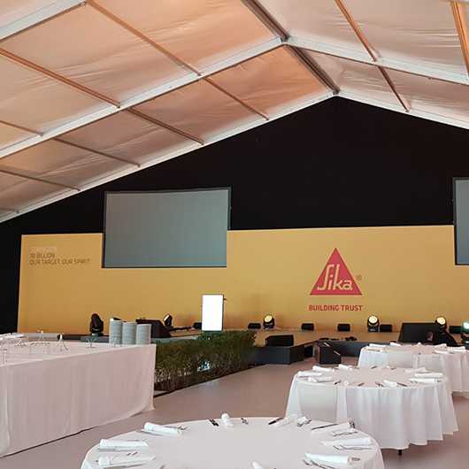 Indoor Event: Sika-Veranstaltung mit Tischen, Bühne und Leinwand.