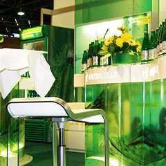 Messestand: Grüner Messestand mit Barhocker, Getränken und Blumendeko. Messe-Design.