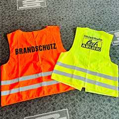 Event Ausstattungen: Ordnerwesten für Brandschutz und Skischule Lech Arlberg. Warnwesten in Orange und Gelb.
