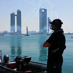 Outdoor Event: Mann mit Headset am Wasser, Boote, Skyline im Hintergrund.