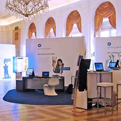 Pop Up Walls Präsentationssysteme: Messestand mit Displays, Tischen und Stühlen unter Kronleuchter.