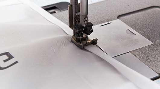 Konfektionierung: Detailaufnahme einer Nähmaschine beim Nähen von Stoff.