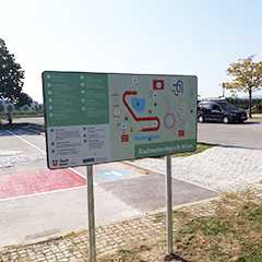 Schild Radmotorikpark Wien. Gebäude und Fahrzeuge im Hintergrund. Orientierungstafel.