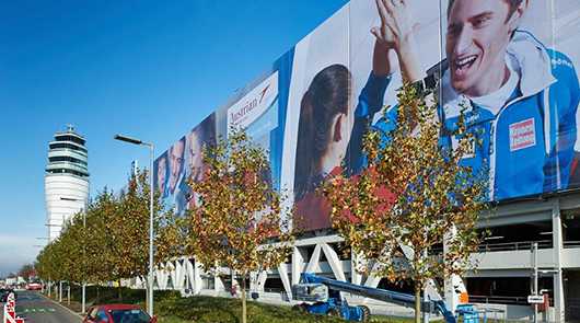 Fassadenwerbung am Flughafen Wien. Großflächige Werbung an Fassade mit Tower im Hintergrund.