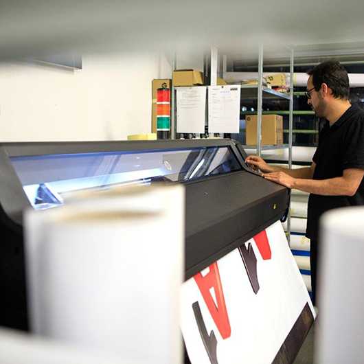 Mann bedient Großformatdrucker. Erfolgsrezept für Druckqualität. Über uns.