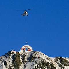 Helikopter montiert Messe-Zelt auf schneebedecktem Gipfel. Messen hoch hinaus.