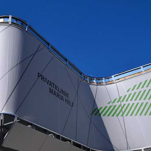 Fassadenverkleidung Privatklinik Maria Hilf. Moderne Fassade mit Schriftzug und grünen Akzenten.